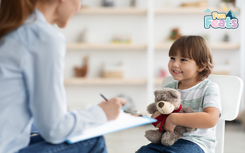 Smiling child holding a teddy bear while talking to a therapist