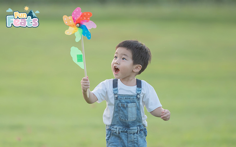 Excited young boy playing outdoors with a colorful pinwheel on a grassy field.
